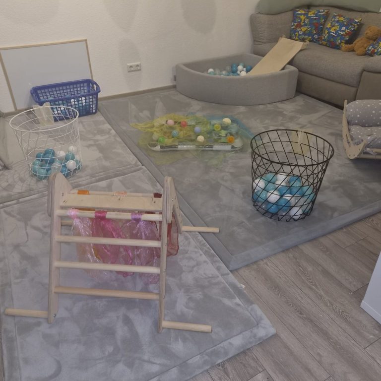 Aufbau für eine Gruppenstunde in der Krabbelwiese Baden-Baden Spielzimmer mit verschiedenen Spielmaterialien auf einem grauen Teppich.