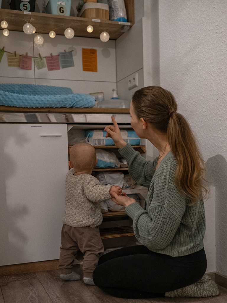 Kinderschutz Krabbelwiese Baden-Baden Mutter zeigt einem Baby in einem gemütlichen Raum Dinge im unteren Regal.