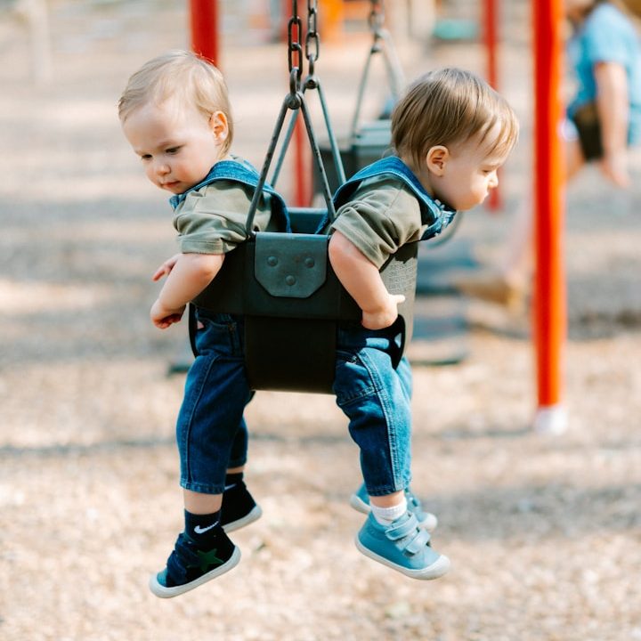 Zwei kleine Kinder in einer Doppelschaukel auf einem Spielplatz.