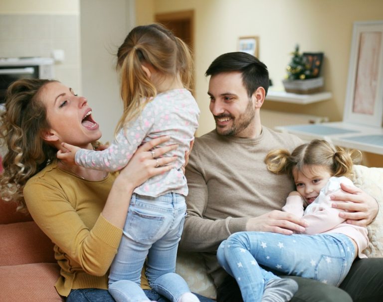 Familie mit zwei Kindern auf der Couch, fröhliche Interaktion und Lachen.
