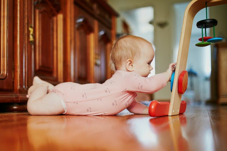 Entwicklung des Kindes Krabbelwiese Baden-Baden Ein Baby liegt auf dem Bauch und spielt an einem Holzspielzeug.