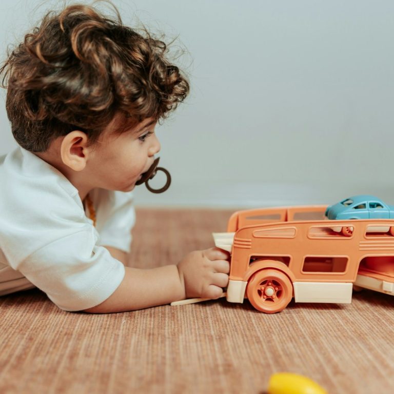 Spiele Krabbelwiese Baden-Baden Ein Kleinkind spielt mit einem orangenen Spielzeugauto auf einem Holzfußboden.