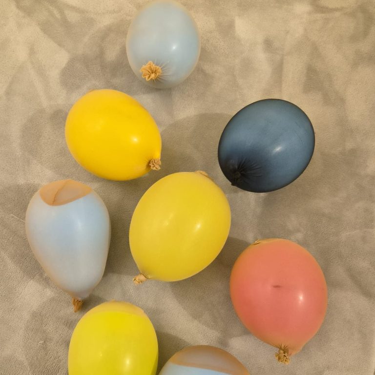 Sinnesimpulse Kleine Krabbler Bunte Luftballons in Gelb, Blau, Pink und Beige liegen auf einem grauen Hintergrund.