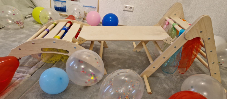 WoodsCraft - Handmade 5in1 Montessori Kletterset Krabbelwiese Baden-Baden Holzspielzeug-Set mit Balanciergerät, bunten Bällen und Luftballons auf dem Boden.