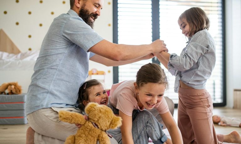 Ein Mann spielt mit vier Kindern im Raum, während sie lachen und spielen.