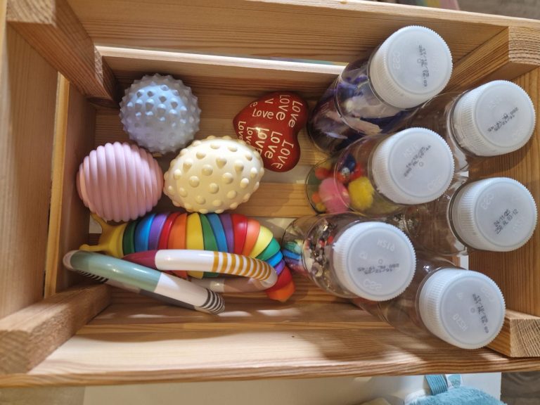 Spielelemente Kleine Krabbler Bunte Spielzeuge und Flaschen in einer Holzkiste.