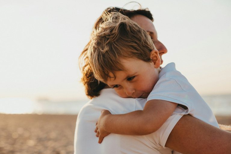 Eine Mutter umarmt ihr kleines Kind am Strand bei Sonnenuntergang.