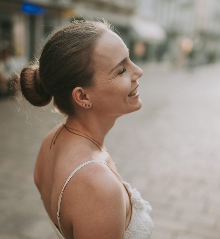 Annika Schröter Über mich Lächelnde Frau mit nach hinten gebundenem Haar, vor einer Stadtlandschaft.