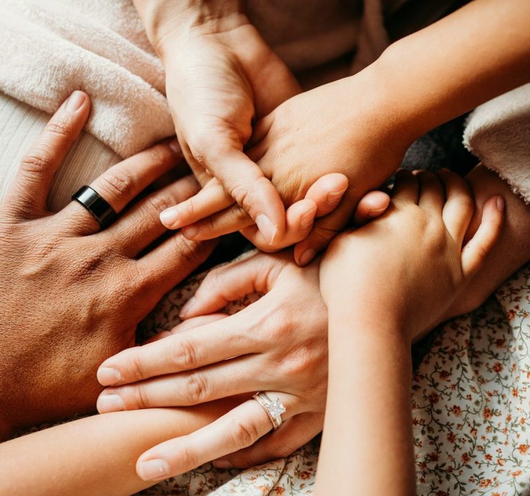 Hände von Erwachsenen und Kindern, die übereinander liegen, symbolisieren Gemeinschaft.