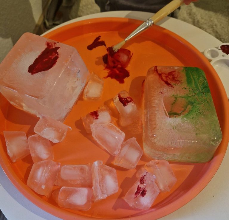 Roter Farbstoff auf Eiswürfeln in einer orangefarbenen Schale.