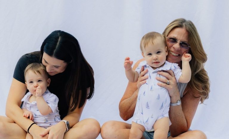 Zwei Frauen sitzen mit zwei Babys in einem hellen, neutralen Hintergrund.