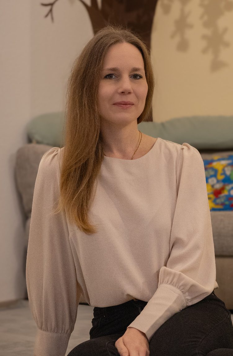 Frau mit langen Haaren in hellem Oberteil, sitzt auf dem Boden vor einem Sofa.