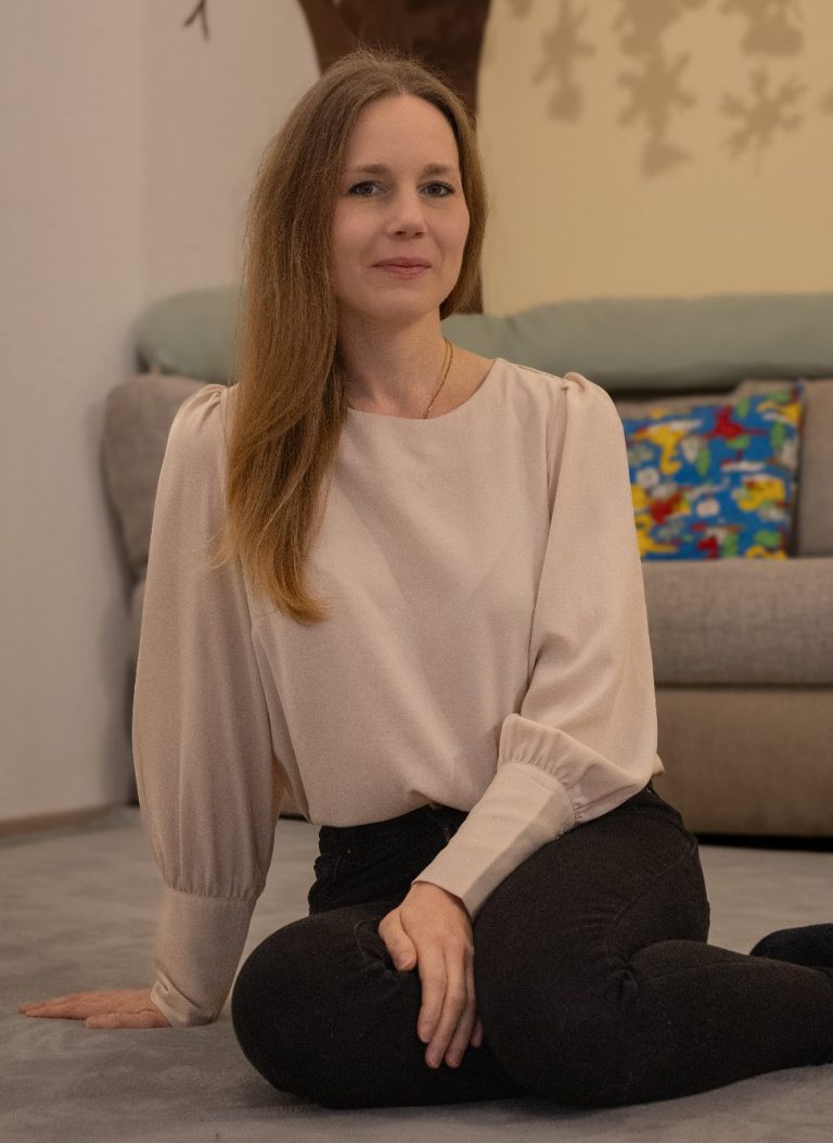 Annika Schröter Krabbelwiese Baden-Baden Frau mit langen, blonden Haaren in einem beigen Oberteil sitzt auf dem Boden.