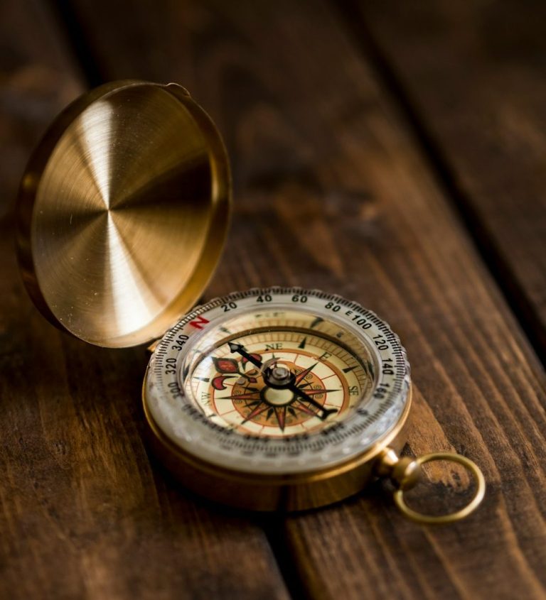 Goldene Kompass auf einem Holztisch, mit detaillierter Skala und Zeiger.