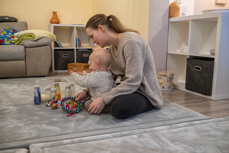 Entwicklung begleiten Krabbelwiese Baden-Baden Eine Mutter spielt mit ihrem Kleinkind auf einem Teppich im Wohnzimmer.