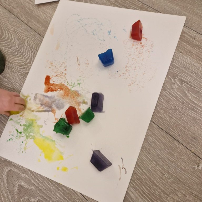 Eis mit Lebensmittelfarbe Malen mit den Sinnen Bunte, geschmolzene Wachsmalstifte auf einem Blatt Papier mit Farbspritzern.