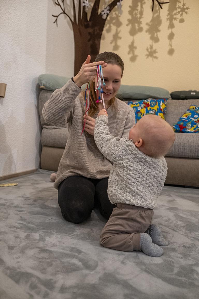 Wertschätzende und achtsame Begleitung Krabbelwiese Baden-Baden Frau spielt mit einem Kleinkind auf einem Teppich, umgeben von bunten Kissen.