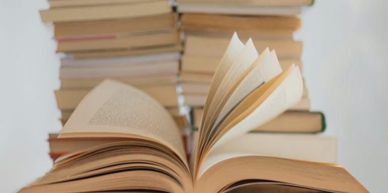 Offene Bücher vor einem Stapel geschlossener Bücher auf einem hellen Hintergrund.